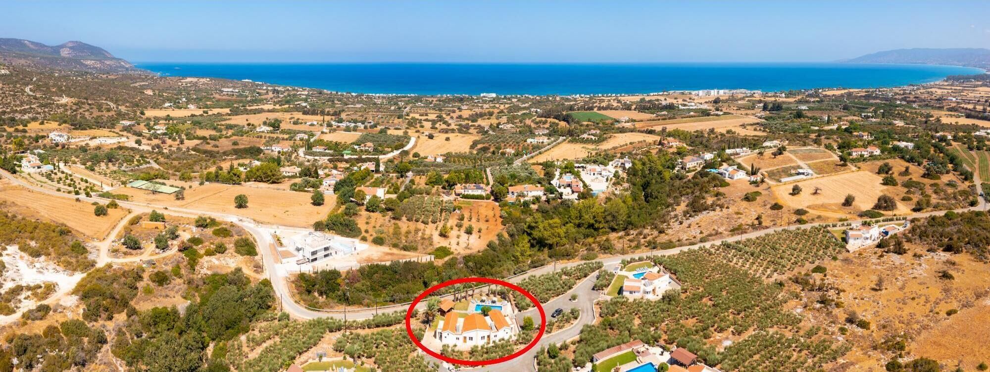 Vue aérienne d’une zone côtière, mettant en évidence une propriété dotée d’une piscine, entourée de champs et d’une végétation clairsemée.
