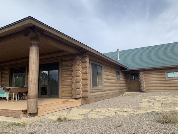 A log cabin with a porch, large windows, and a stone patio.