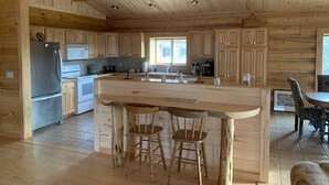 A spacious kitchen with wooden cabinets, a stainless steel refrigerator, a microwave, and a large island with bar stools. - Western Slope Mountain Retreat. Privacy, solitude, incredible views (New Castle)