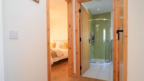Een slaapkamer met een bed, een nachtkastje en een houten deur die leidt naar een badkamer met een douche.