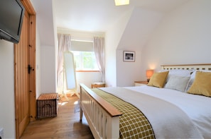 A bedroom with a wooden bed, a bedside table with a lamp, a window with curtains, and a small wooden chest.