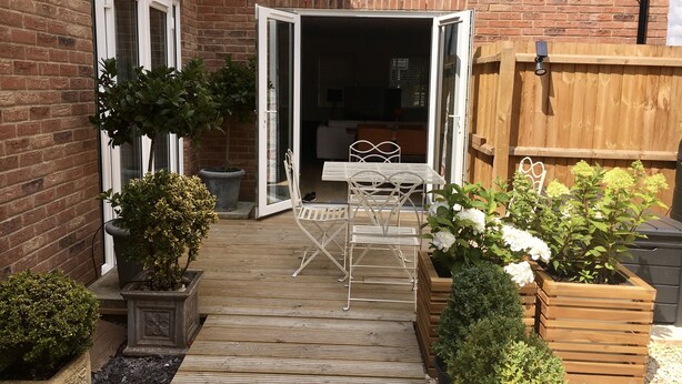 A wooden deck with a table and chairs, surrounded by potted plants and a brick wall. - Entire Stylish Garden Apartment 2 double ensuite bedrooms sleeps 4 Pet friendly  (Wisbech)
