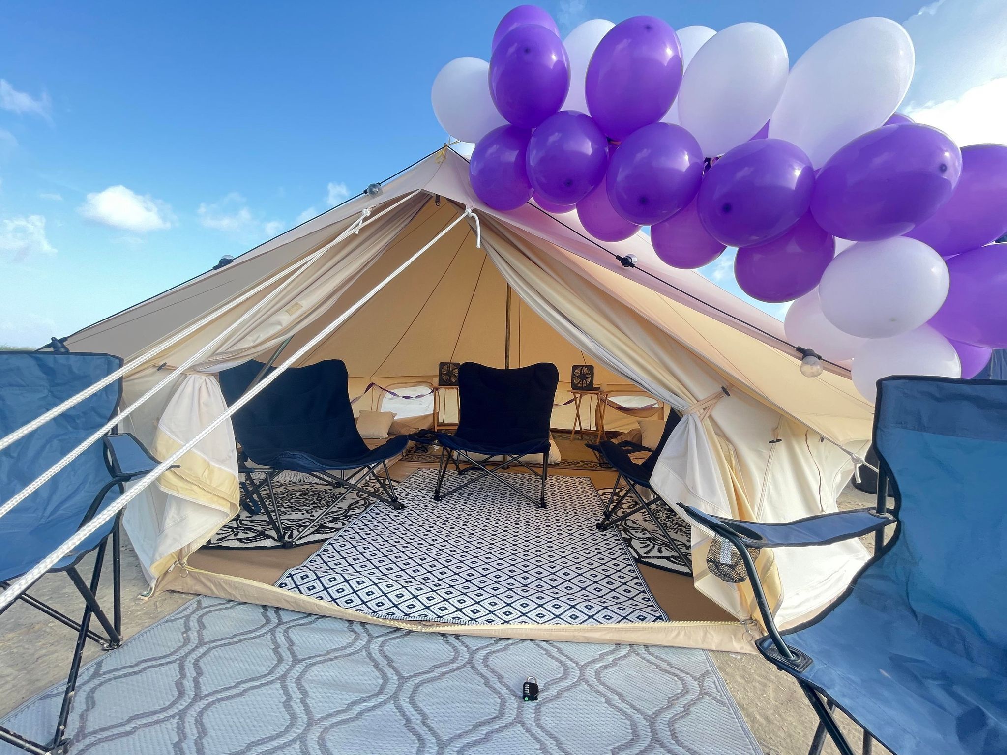 A tent with a bed, two chairs, and a patterned rug.