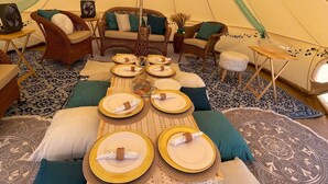 Ein Zelt mit Esstisch für vier Personen, umgeben von Korbmöbeln und gemusterten Teppichen.