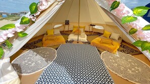 Ein Zelt mit gemütlicher Einrichtung, darunter ein Bett, ein kleiner Tisch und ein gemustertes Teppich.