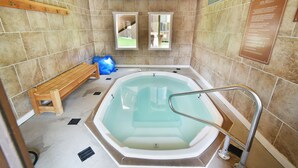 Ein Wellnessraum mit Whirlpool, einer Holzbank und gefliesten Wänden.