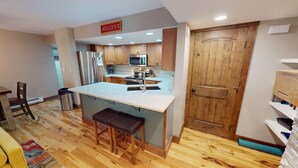 Eine Küche mit Holzausstattung, einem Edelstahlkühlschrank, einer Mikrowelle und einer Holztür.