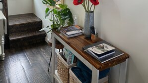 Un soggiorno moderno con una scala in legno, una TV a parete e un vaso con fiori rossi su un tavolo consolle in legno.