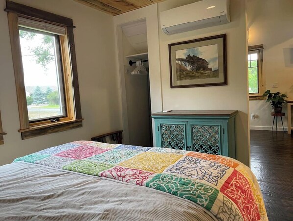 Une chambre avec un grand lit, une fenêtre, une armoire de couleur turquoise et un tableau accroché au mur.