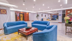 Eine geräumige Lobby mit blauen Sesseln, einem Holztisch und einer Rezeption.