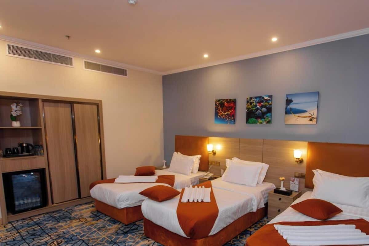 A hotel room with three beds, a minibar, and artwork on the wall.