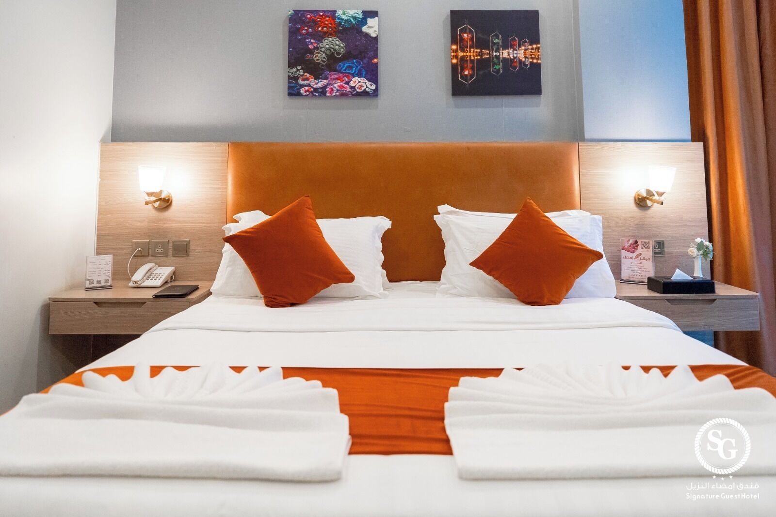 Ein Hotelzimmer mit einem großen Bett, zwei Kissen, einem Nachttisch mit Telefon und einer Nachttischlampe sowie einem Bild an der Wand.