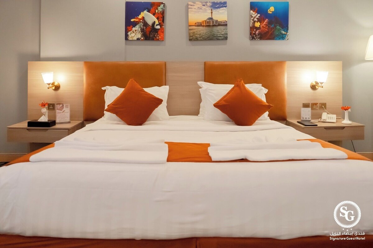 A hotel room with a large bed, two nightstands, a wooden headboard, and artwork on the walls.