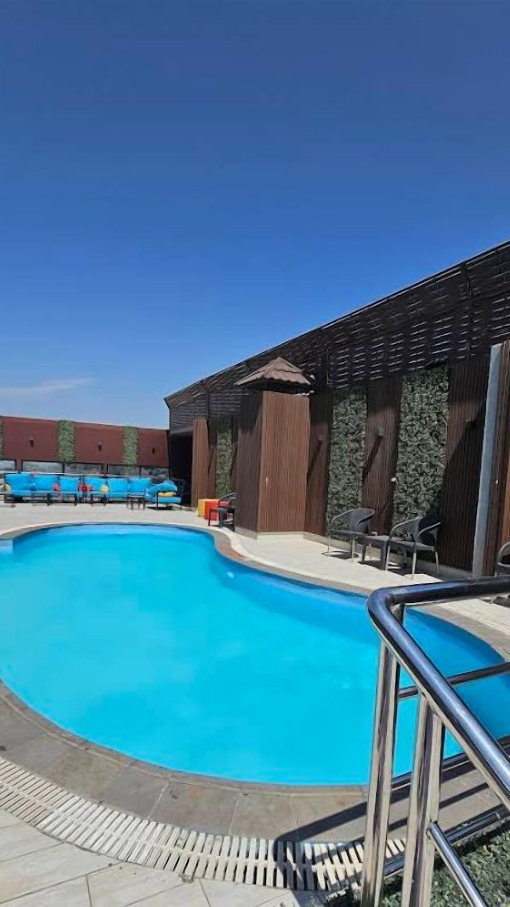 Une piscine entourée d’une rambarde en métal, elle-même bordée d’un bâtiment dont l’extérieur est en bois et le sol carrelé.