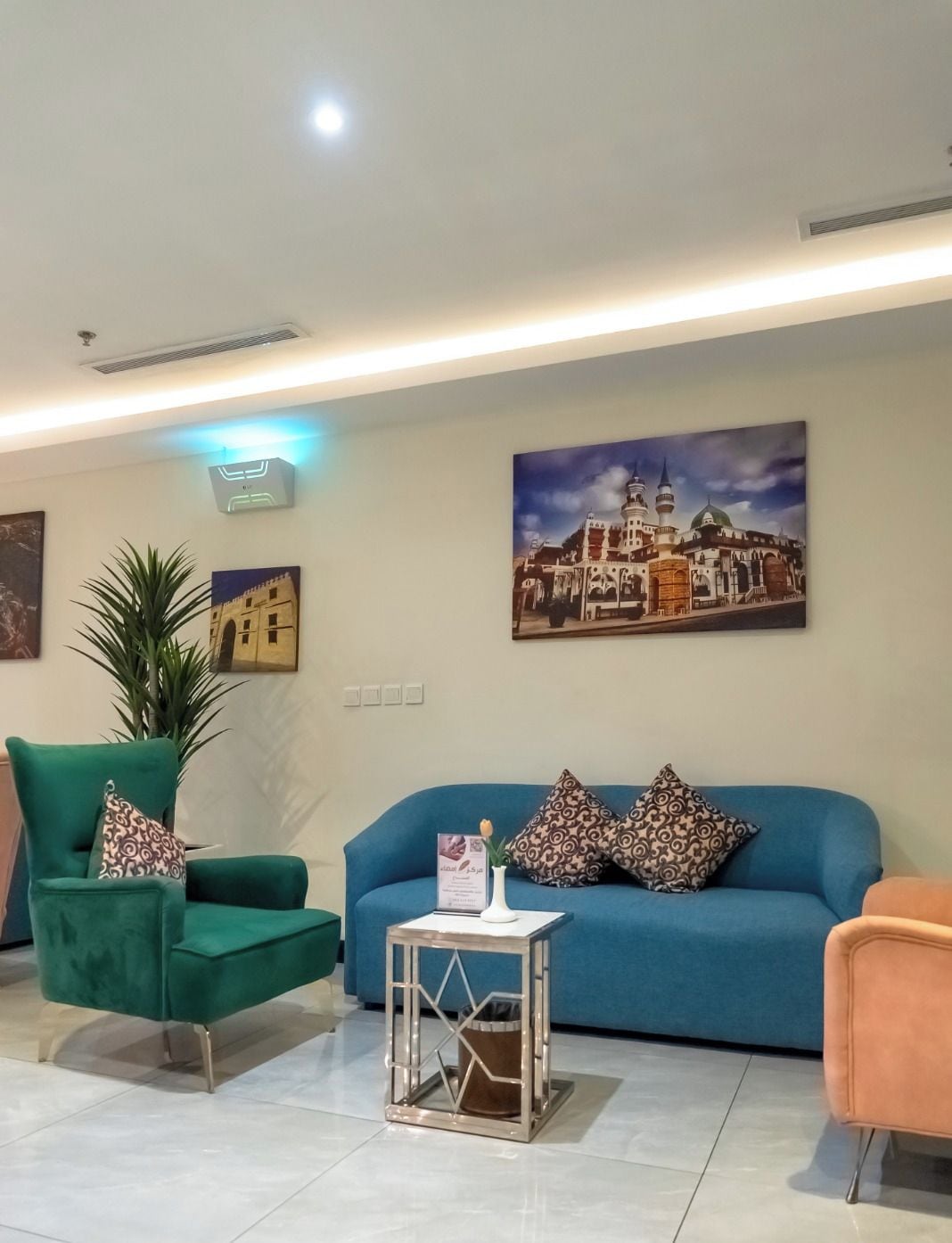 A modern living room with a blue sofa, green armchair, and orange armchair. There are decorative pillows and a small table with a vase.