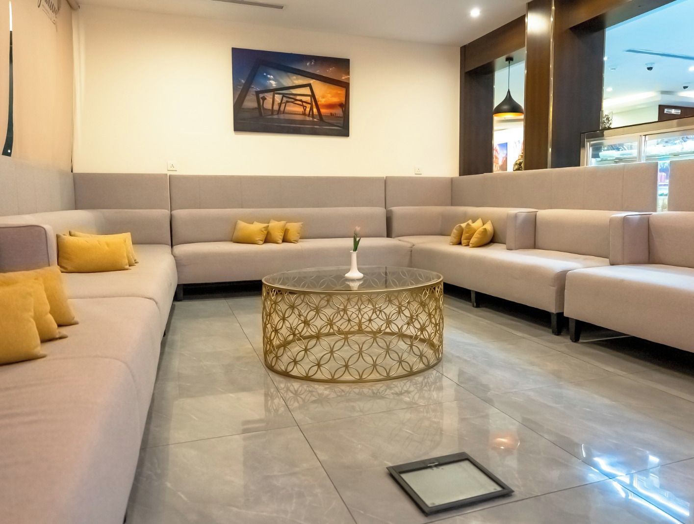 Un moderno hall de hotel con un amplio sofá modular, una mesa de centro de vidrio decorativa y una obra de arte enmarcada en la pared.