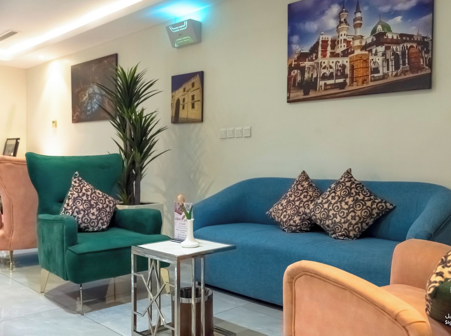 Un vestíbulo de hotel moderno con un sofá azul, un sillón verde y una pequeña mesa con un florero.