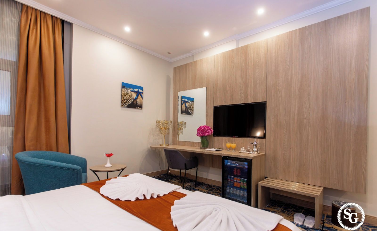 Ett hotellrum med en säng, ett skrivbord, en stol, en TV och en minibar.