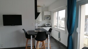 Uma cozinha moderna com uma mesa de jantar, cadeiras, uma televisão e uma janela com cortinas.