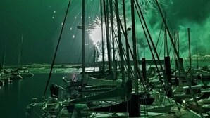 Um cais com barcos atracados e fogos de artifício ao fundo.