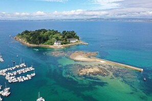 An island with a white building surrounded by lush greenery and clear blue waters. - Apartment near the ocean and beaches (Douarnenez)
