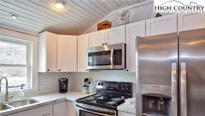 Una cocina moderna con armarios blancos, electrodomésticos de acero inoxidable, horno empotrado y dispensador de agua.