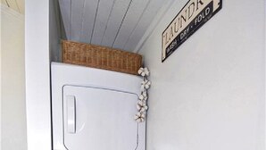 Pequeña lavandería con lavadora y secadora blancas, una cesta encima de la secadora, y un cartel que dice 'LAVANDERÍA - DOBLE'.
