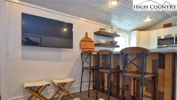 Una cocina moderna con taburetes de madera, un televisor de pantalla plana montado en la pared y una mesa de madera rústica.