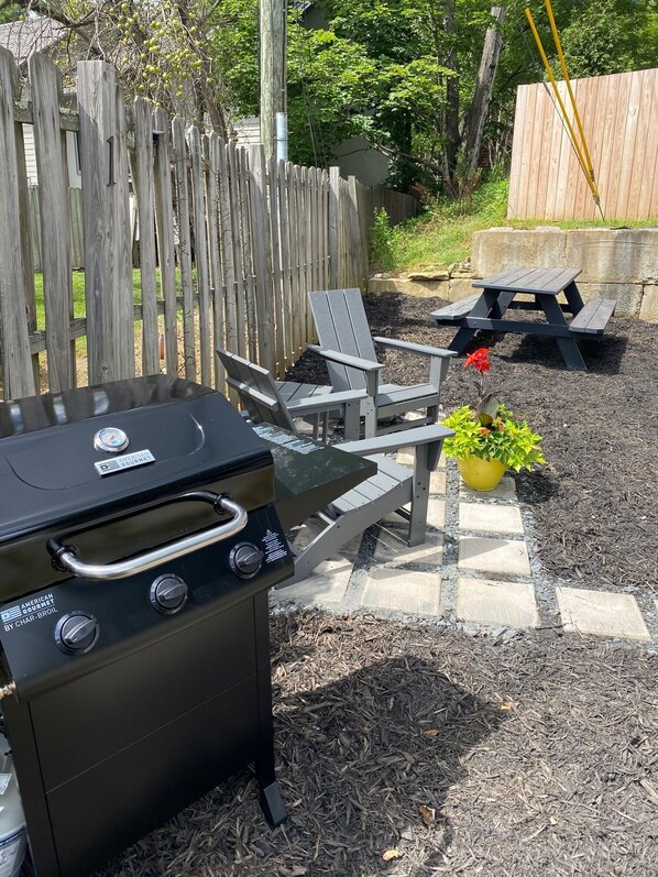 A backyard with a grill, patio furniture, and a wooden fence.