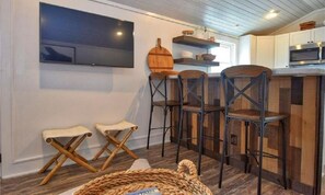 A modern kitchen with wooden bar stools, a flat-screen TV mounted on the wall, and a rustic wooden table. - Urban Oasis on King Street! (Boone)