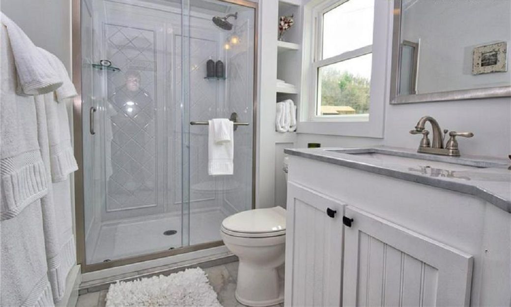 A modern bathroom with a glass-enclosed shower, a white toilet, and a vanity with a sink and mirror.