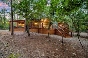 A wooden cabin with a deck and stairs, surrounded by trees.