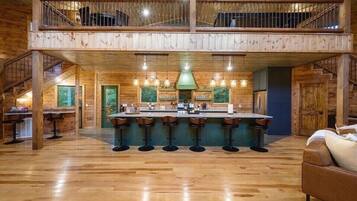 A spacious wooden interior with a central bar area, multiple seating options, and a staircase leading to an upper level.