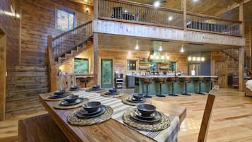 A spacious wooden interior with a dining area set for six, a kitchen with a bar, and a staircase leading to a loft.