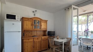 A compact kitchen with wooden cabinets, a white refrigerator, and a dining area with a table and chairs. - FRONTLINE APARTMENT FACING THE SEA (Argelès-sur-Mer)