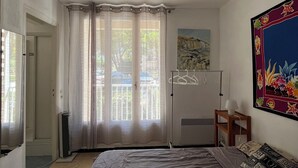 A bedroom with a bed, a window with curtains, a radiator, a wall-mounted lamp, and a painting. - FRONTLINE APARTMENT FACING THE SEA (Argelès-sur-Mer)
