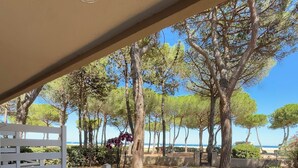 An outdoor patio with a table set for two, surrounded by white plastic chairs, overlooking a coastal area with trees and a clear sky. - FRONTLINE APARTMENT FACING THE SEA (Argelès-sur-Mer)