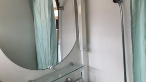 Een badkamer met een ronde spiegel, een handdouche en een glazen plank.