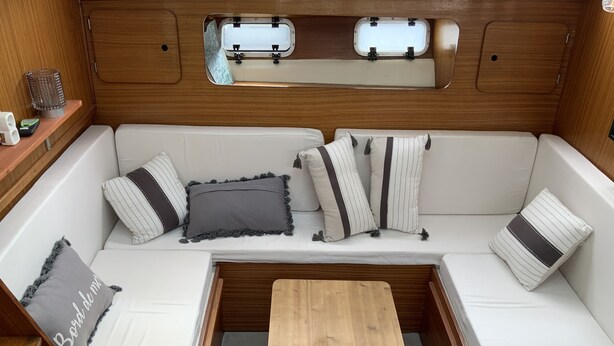 Een knus interieur van een camper, met een houten tafel, comfortabele zitplaatsen en een klein raam.