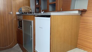 Een kleine keuken met houten kastjes, een inbouwoven, een koelkast en een spoelbak met kraan.