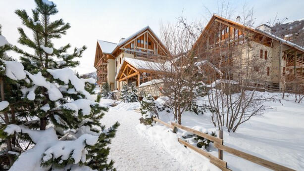 Una cabaña de madera con fachada de piedra, rodeada de árboles cubiertos de nieve y un cielo despejado.