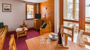 Una habitación acogedora con detalles de madera, una cama, una mesita con copas de vino, un televisor y una ventana con vistas a un paisaje nevado.