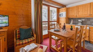 Ein gemütlicher, blockhausähnlicher Raum mit Holzvertäfelung, einem Esstisch mit Stühlen, einem Sofa mit Karokissen, einem Fernseher und einer Küchenzeile mit Holzausstattung und einer Mikrowelle.