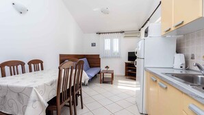 A compact kitchen with a refrigerator, stove, and sink. There is a dining table with chairs and a bed with a headboard. - Holiday apartment with mountain view (Baška)