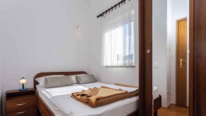 A neatly made bed with a brown blanket, a bedside lamp, and a window with sheer curtains. - Holiday apartment with mountain view (Baška)