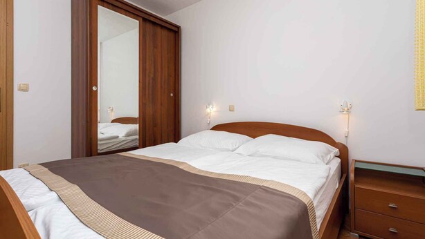 A bedroom with a bed, wooden wardrobe, bedside table, and wall-mounted light.