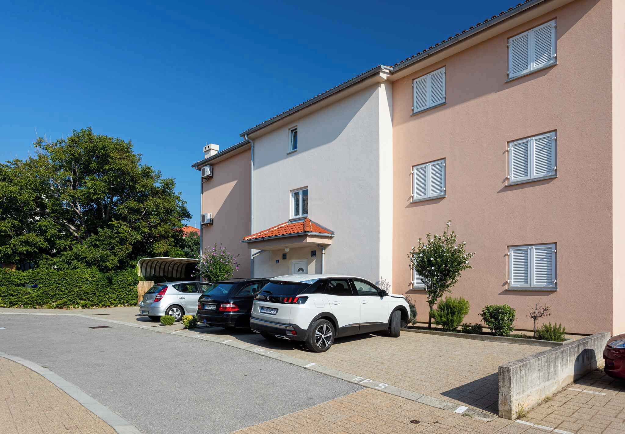 Un edificio residencial con fachada color beige, múltiples ventanas con contraventanas y un coche blanco estacionado en la entrada.