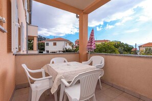 A balcony with a table and chairs, overlooking a residential area with houses and a mountain in the background. - Holiday apartment close to the city centre and the beach (Baška)