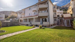 Un immeuble résidentiel à plusieurs étages, doté de balcons, d’une cour pavée et surplombant un paysage montagneux.