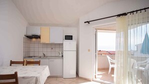 Une cuisine compacte avec des meubles blancs, un four à micro-ondes et un réfrigérateur. On y trouve une table à manger avec des chaises, ainsi qu’un balcon avec vue.